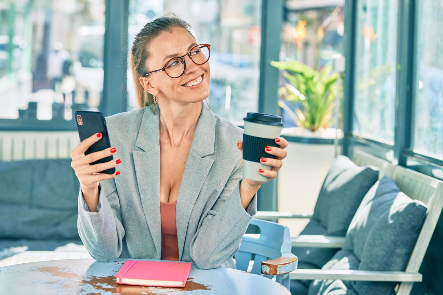 Woman smiling while holding her phone and coffee